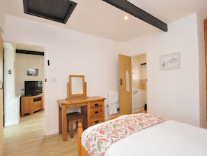 A bedroom with a bed, a desk with a chair, a television, and a bathroom visible through an open door.