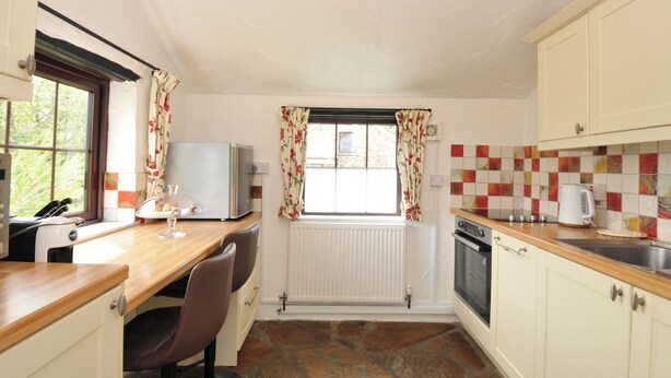 A compact kitchen with a stone floor, a refrigerator, a stove, and a window with curtains.