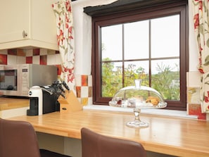 A kitchen with a microwave, knife block, and a window with a view of greenery.