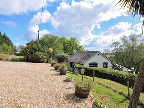 A house with a gravel driveway, surrounded by greenery and a clear sky.