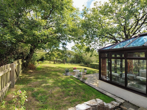 A conservatory with a glass roof, surrounded by a garden with a wooden fence and potted plants.