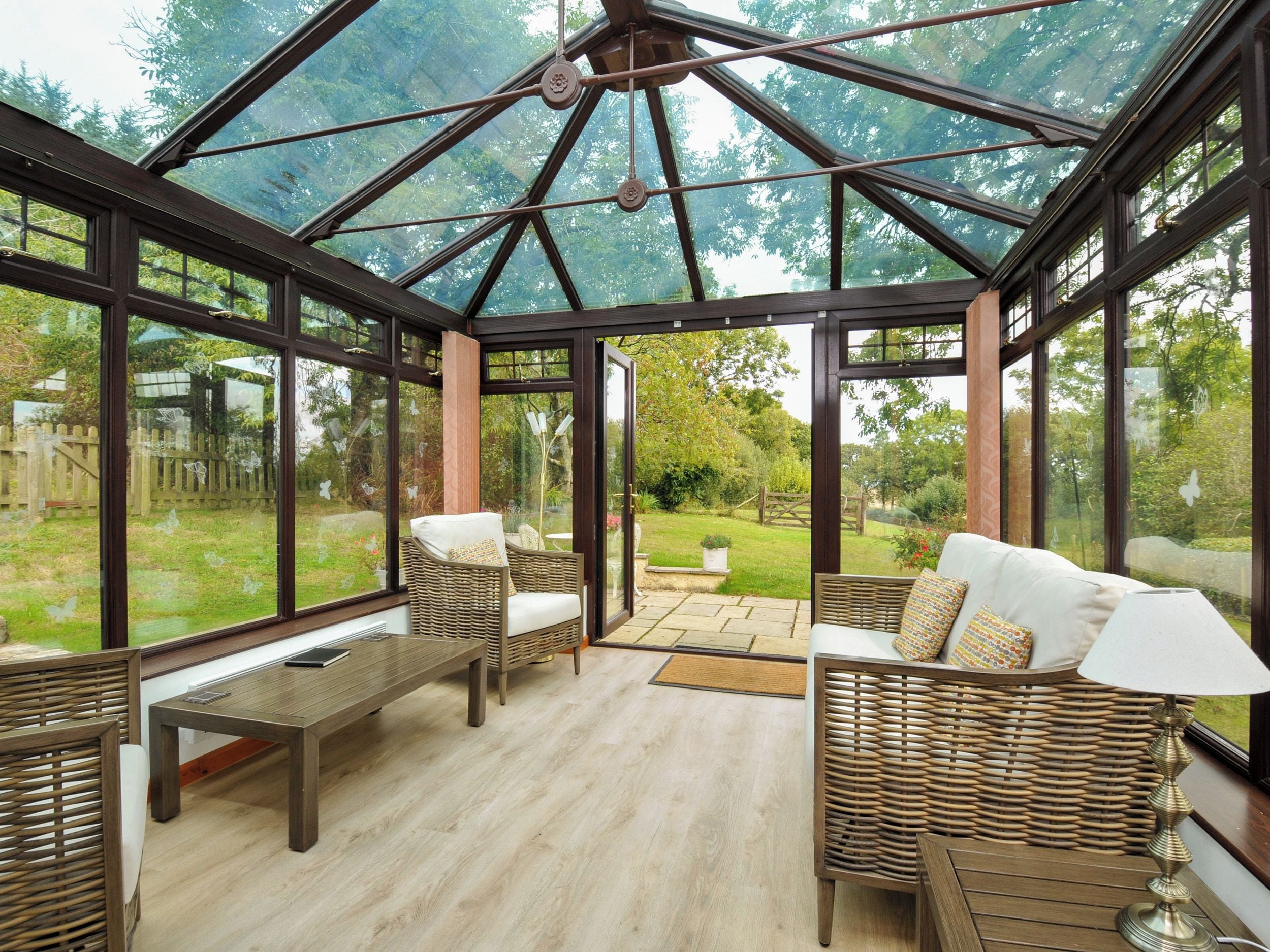 A conservatory with wicker furniture, a wooden table, and a view of the garden.
