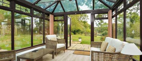 A conservatory with wicker furniture, a wooden table, and a view of the garden.