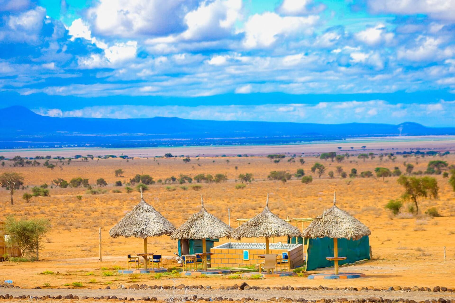 A desert landscape with thatched-roof huts and a view of distant mountains.