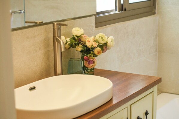 A bathroom with a white sink, a wooden countertop, and a vase of flowers.