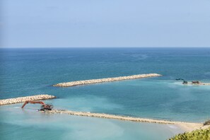 A coastal area with a clear view of the sea, a rocky breakwater, and construction machinery.