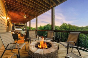A covered deck with a stone fire pit, outdoor seating, and a view of the surrounding forest. - Indoor Pool! Lake Access! Hot Tub! (Branson)