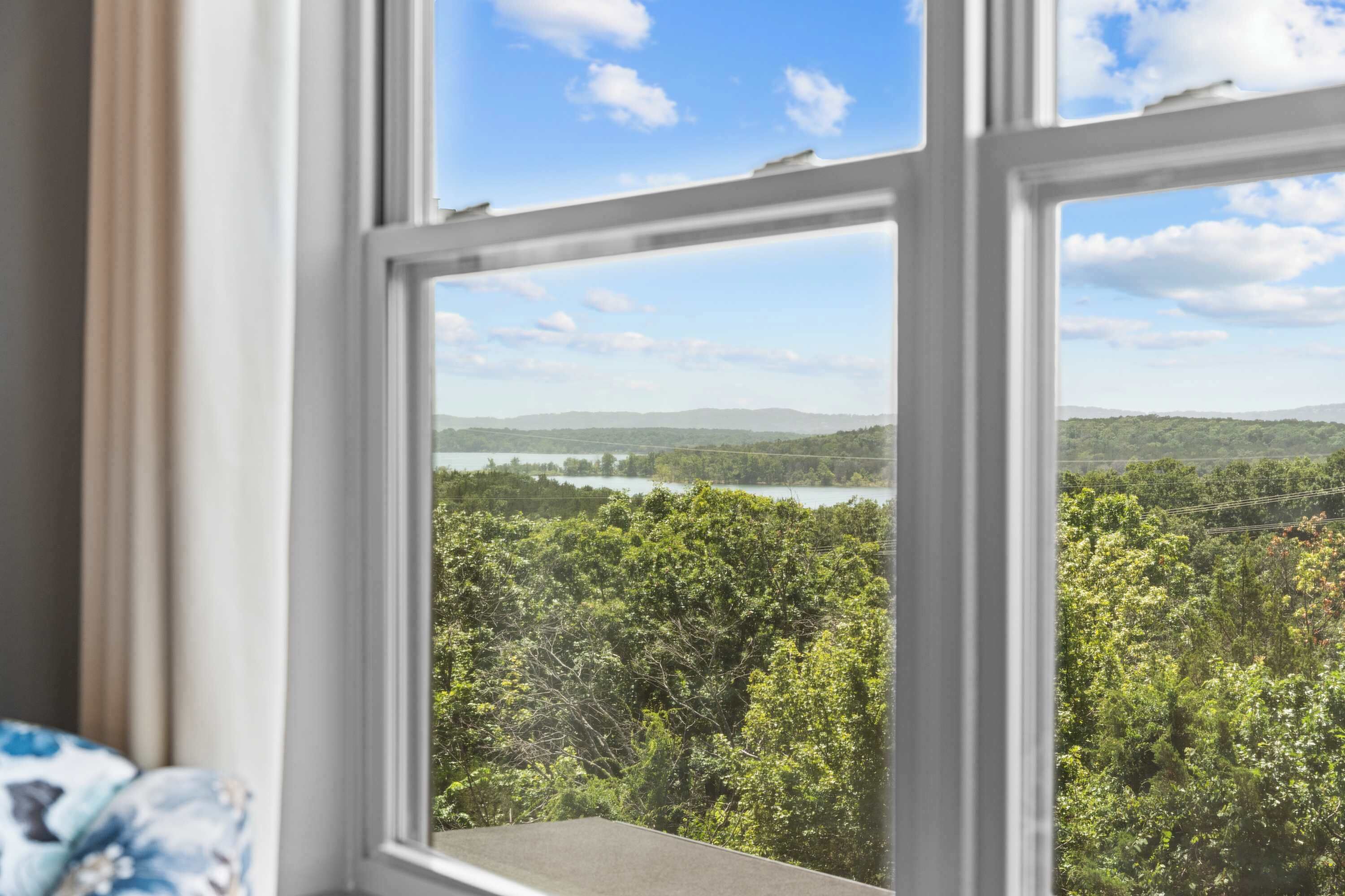 A window with a view of a forested landscape and a body of water.