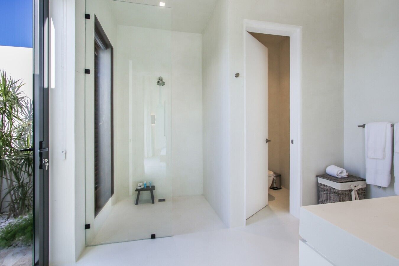 Un baño moderno con cabina de ducha de vidrio, un taburete pequeño y una cesta de mimbre.