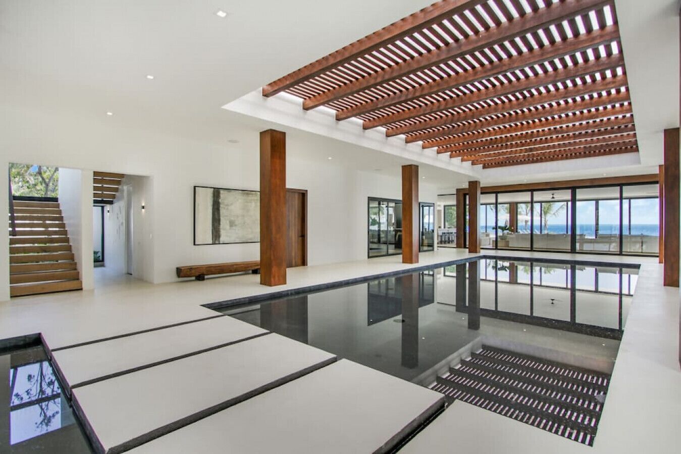 A spacious indoor area with a reflective floor, wooden ceiling beams, and large windows offering a view of the sea.