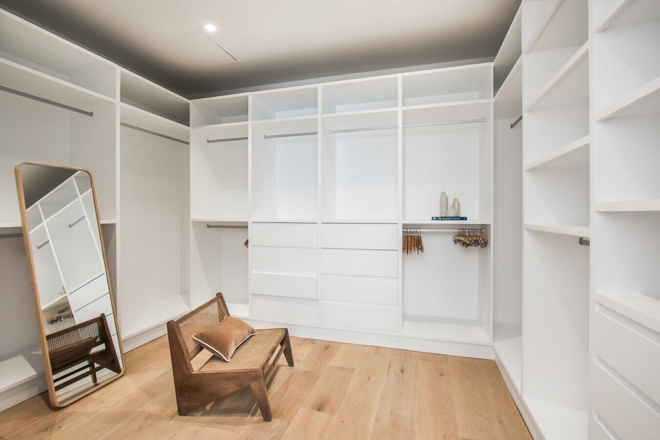 Un dressing accessible sans porte, doté d’étagères ouvertes, d’un miroir et d’un banc.