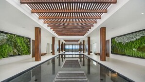 Een moderne hotellobby met een centraal gelegen reflectiepoel, houten plafondlatten en verticale tuinen aan de wanden.
