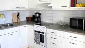 A modern kitchen with white cabinets, a built-in oven, a microwave, and a coffee maker. - Modern flat centrally located (Helsinki)