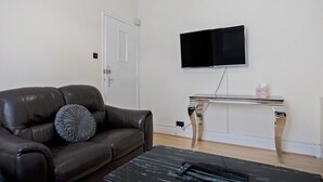 Olohuoneessa on nahkasohva, sohvapöytä, seinälle asennettu televisio ja pieni valkoinen kaappi.