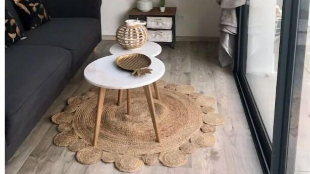 Moderni olohuone, jossa on tumma sohva, pieni valkoinen pöytä, jonka päällä on koristeellinen kulho, pyöreä peili ja kudottu matto.