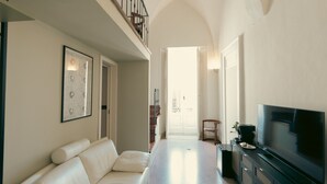 Amplia sala de estar con techo alto, un sofá blanco, un televisor de pantalla plana y una escalera que lleva a un nivel superior.
