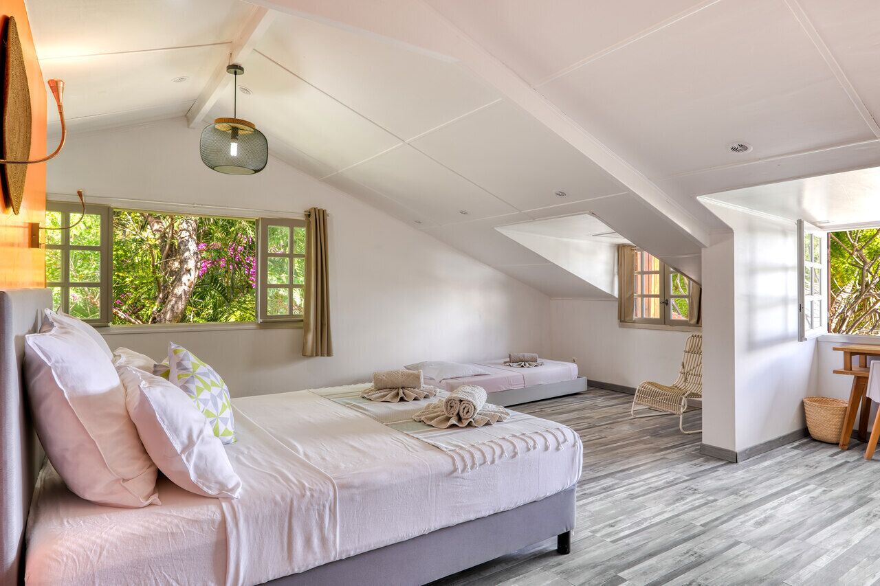 Un dormitorio con dos camas, suelo de madera y ventanas amplias con vistas a árboles.