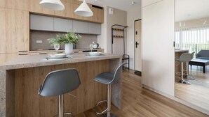 Une cuisine moderne avec des meubles en bois, un îlot central doté de tabourets de bar, un éclairage suspendu et une vue sur l’espace repas.