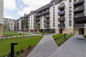 Un edificio residencial moderno de varios pisos con balcones, un patio central y un camino pavimentado.