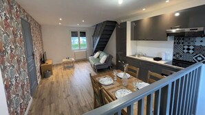 Una cocina moderna con armarios oscuros, un comedor con mesa de madera dispuesta para cuatro personas y una escalera que sube a un nivel superior.