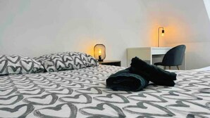 Un dormitorio con una cama, dos almohadas, un escritorio, una silla y dos lámparas fijadas a la pared.