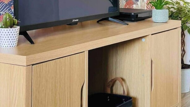 Un televisor sobre un mueble de madera con un estampado floral en el fondo.