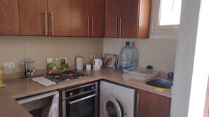 Une cuisine compacte dotée de meubles en bois, d’un lave-linge, d’une machine à café et d’un grand distributeur d’eau.