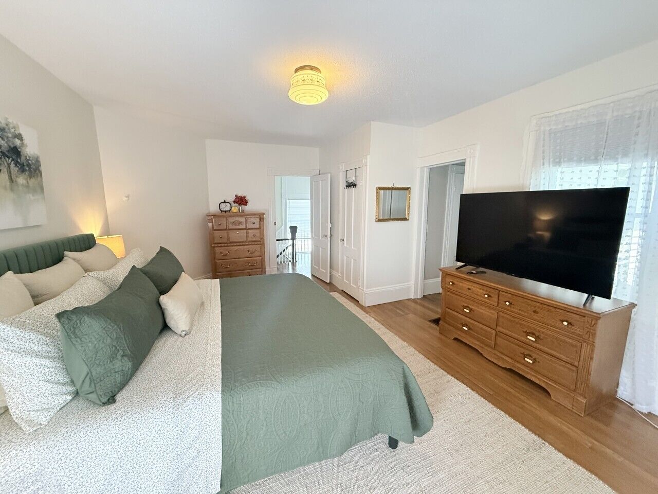 A bedroom with a bed, dresser, TV, and a door leading to another room.