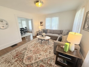 Ein Wohnzimmer mit Sofa, Couchtisch und Lampe. An der Wand hängt eine Uhr und auf dem Boden liegt ein Teppich.