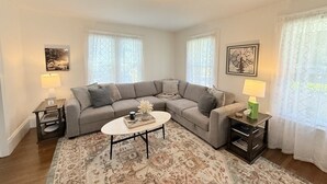 A living room with a sectional sofa, a round coffee table, and two lamps on side tables. - Prime West Hartford Center Location: Historic Gem (West Hartford)