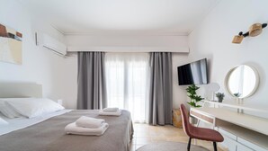 Ett hotellrum med en säng, ett skrivbord, en stol, en TV, en spegel och gardiner.