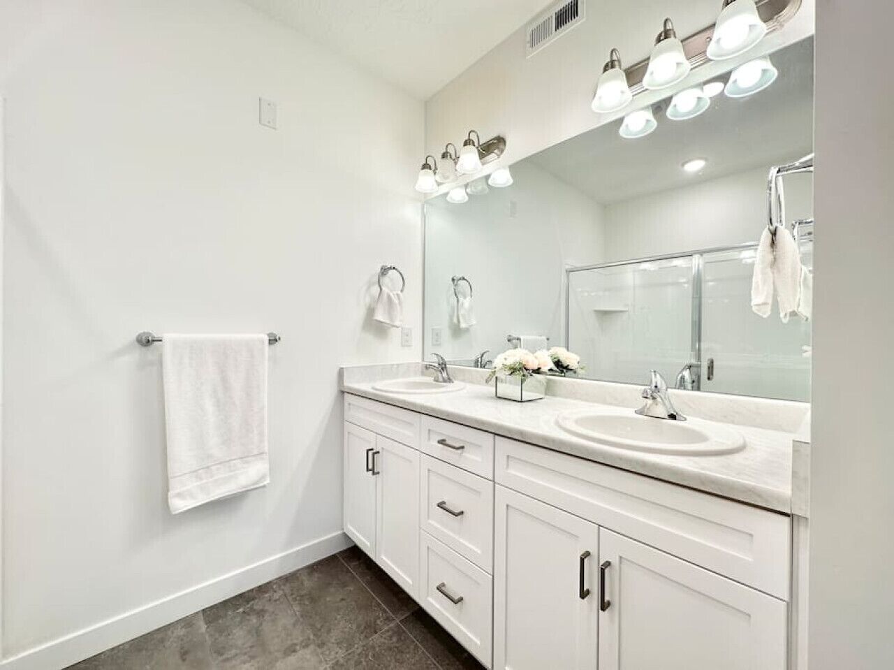 A modern bathroom with two sinks, a large mirror, and a towel rack.