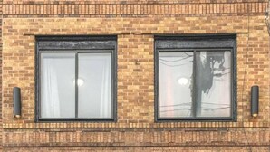 Un edificio de ladrillo con dos ventanas, cada una enmarcada en negro y con cortinas.