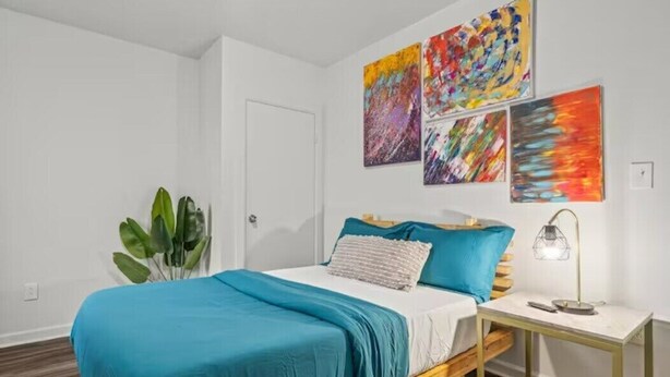 Un dormitorio con una cama, una mesita de noche, una lámpara y tres cuadros abstractos en la pared.