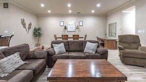 Un salon avec un canapé en cuir marron, une table basse en bois, un coin repas avec des chaises et un téléviseur fixé au mur.