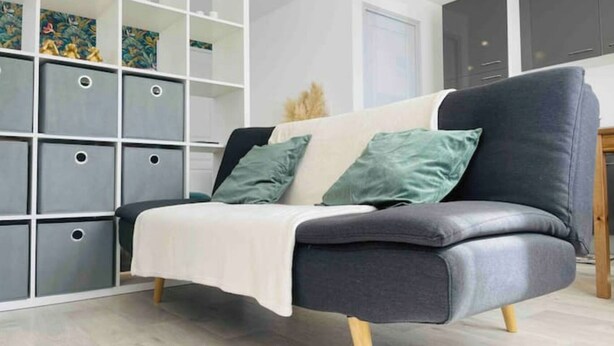 Un salon moderne avec un canapé gris, deux coussins, un plaid blanc et un meuble de rangement doté de plusieurs compartiments.