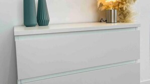 Une commode blanche, sur laquelle sont posés deux vases turquoise et un luminaire décoratif.