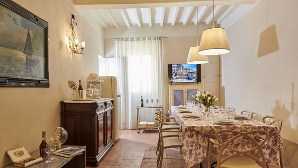 A dining area with a table set for four, a television mounted on the wall, and a decorative wall sconce.