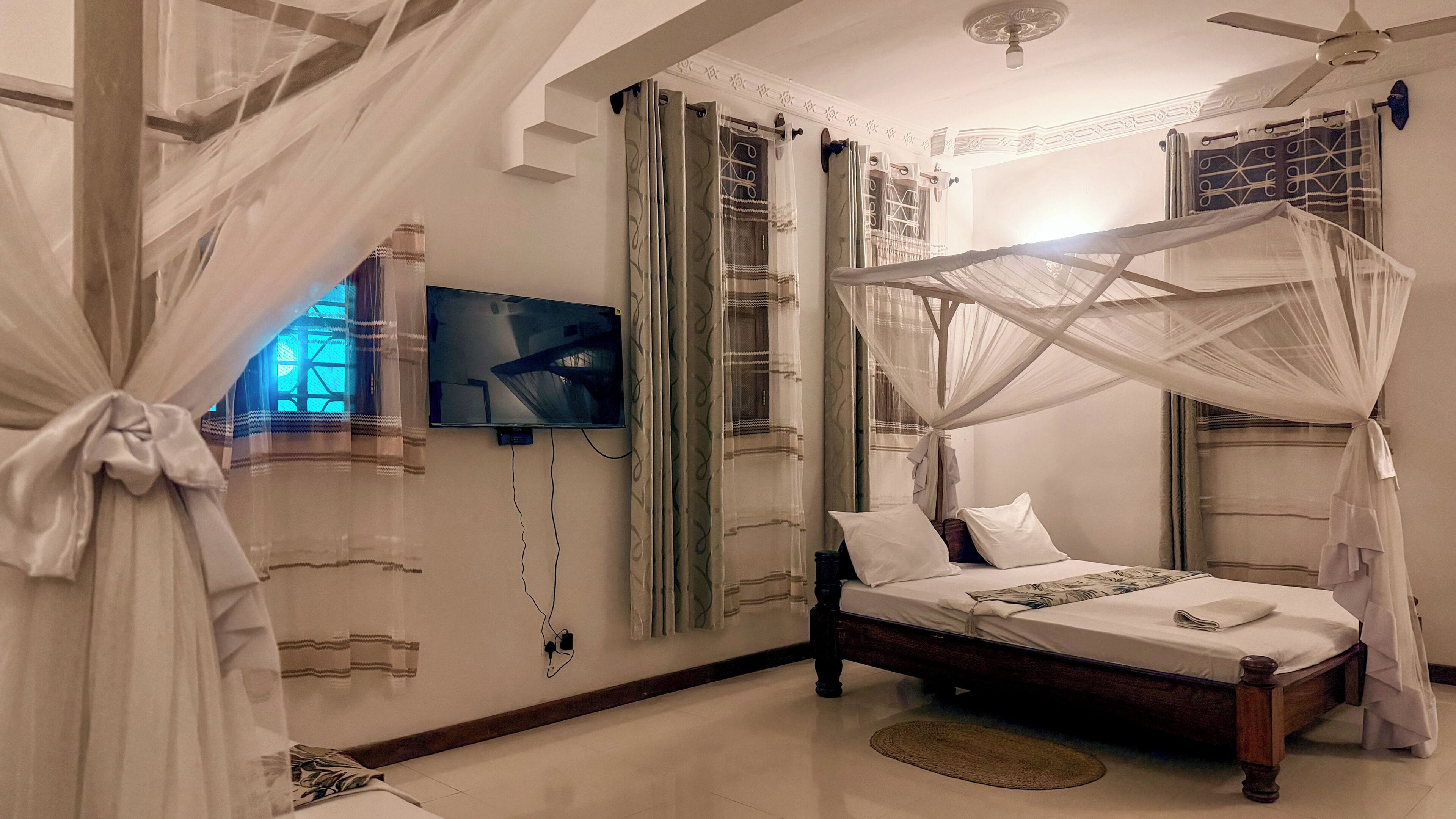 Un dormitorio con cama, cortinas, televisor y ventilador de techo.