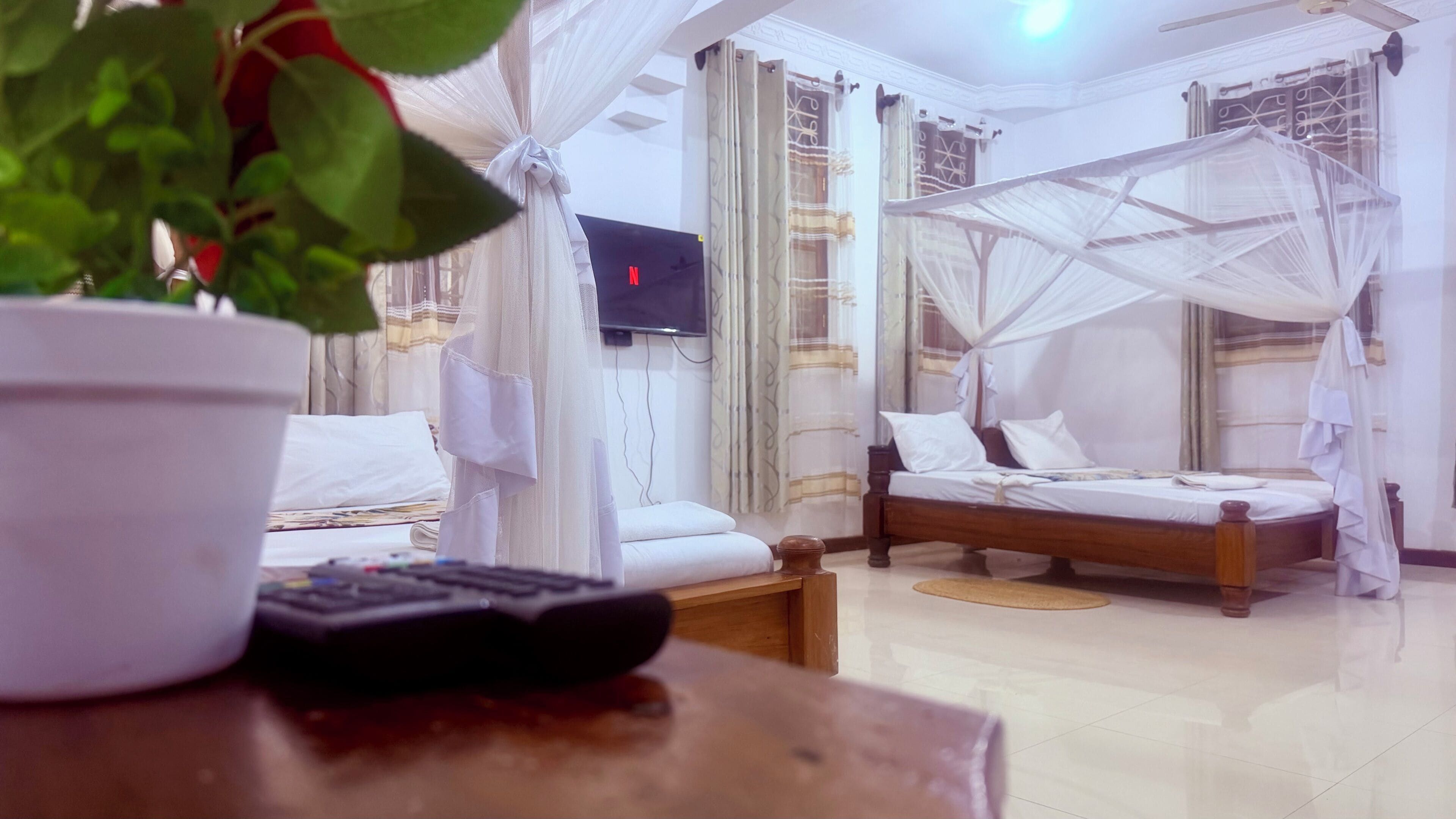 Ett hotellrum med en säng, en tv, en fjärrkontroll och en krukväxt.