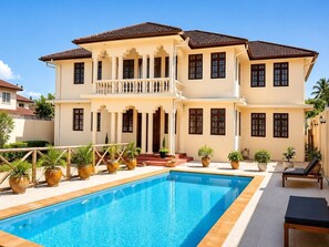Uma casa de dois andares com piscina, plantas em vasos e área de estar externa.