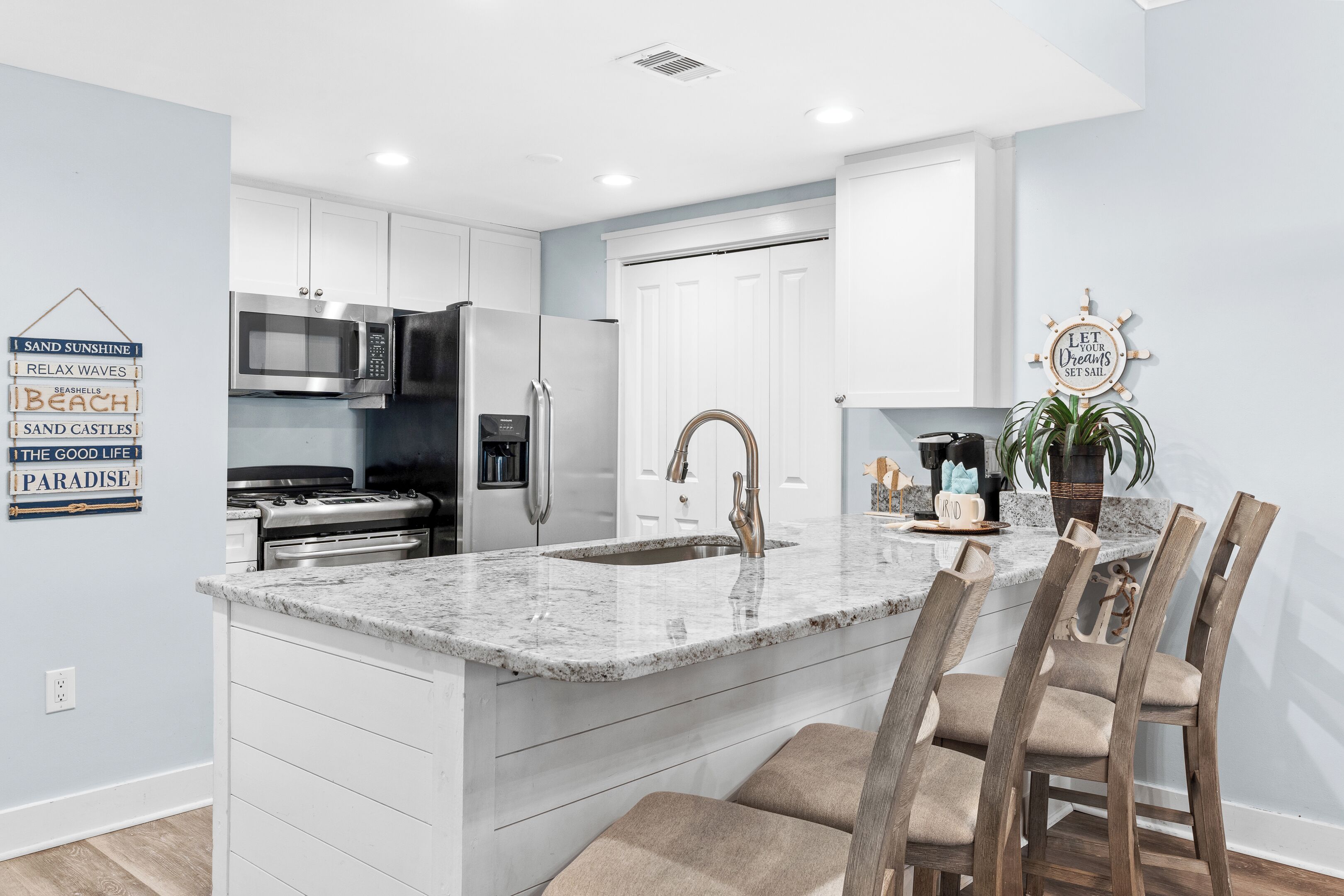 A modern kitchen with white cabinetry, a stainless steel refrigerator, a built-in oven, and a granite countertop.