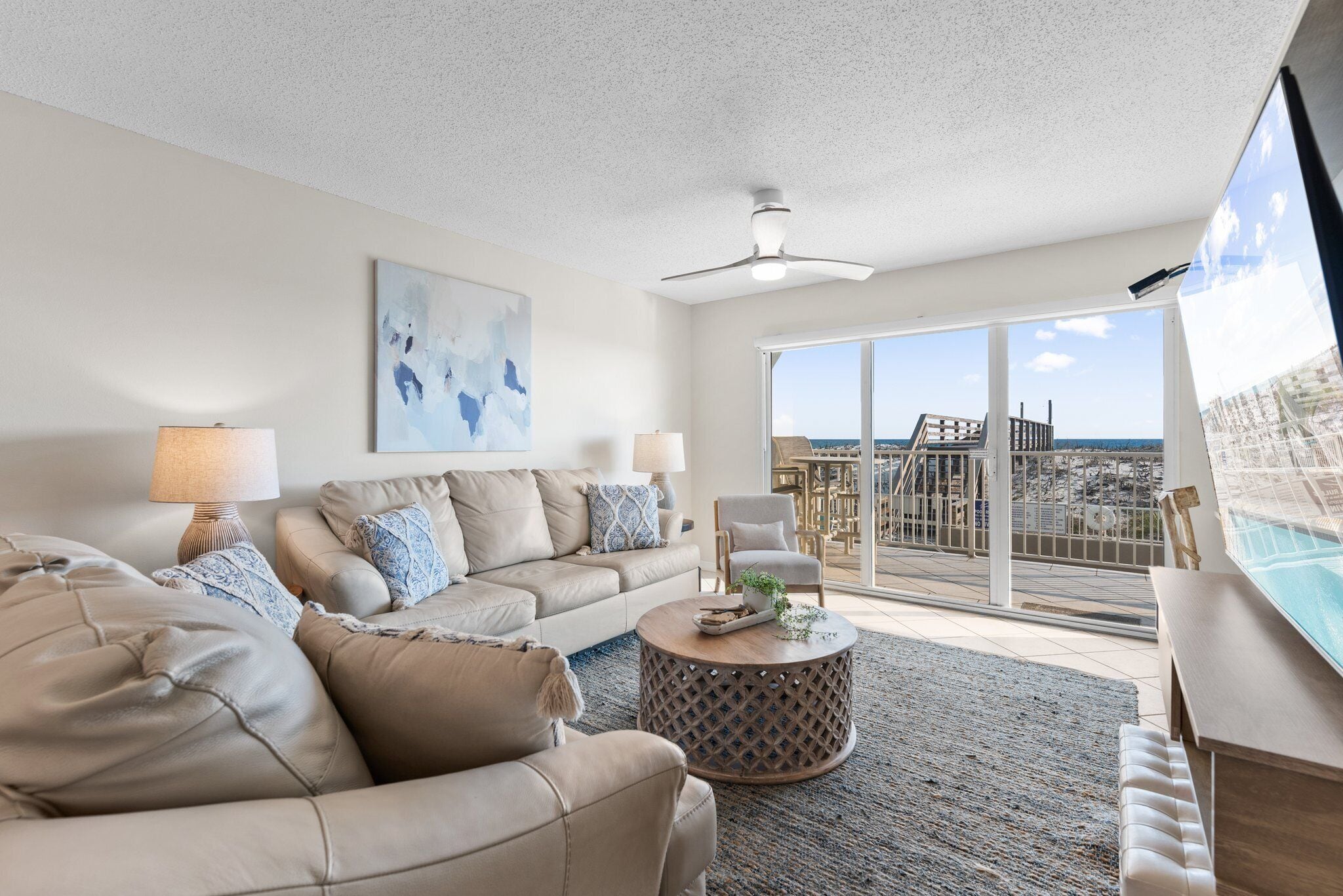 A spacious living room with a large sofa, a coffee table, and a view of the ocean through large sliding glass doors.