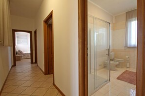 Ein Hotelkorridor, der zu einem Badezimmer mit Duschkabine, Toilette und Waschbecken führt.