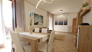 Un coin repas avec une table en bois et des chaises blanches, un vase avec des plantes et un tableau au mur.