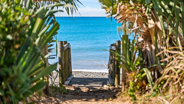 Un sentier en bois mène à une plage où l’eau est d’un bleu cristallin.