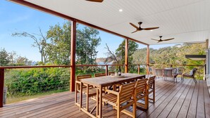 Une terrasse en bois avec une table et des chaises, un ventilateur de plafond et une vue sur le paysage environnant.