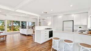 Une cuisine moderne avec des meubles blancs, un îlot central doté de tabourets et un coin repas comprenant un canapé et des chaises blancs.