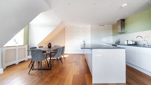 A modern kitchen with a central island, white cabinetry, and a dining area with a wooden table and chairs. - The South Hampstead Collection (London)