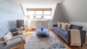 A modern loft apartment with a loft bed, a grey sofa, a round coffee table, and a large window providing natural light. - The South Hampstead Collection (London)